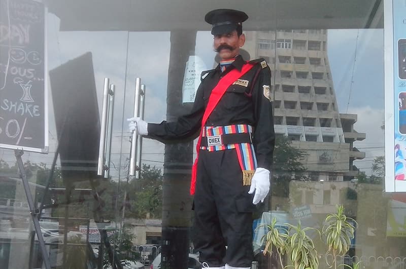 An Omax doorman in ceremonial uniform at a glass entrance